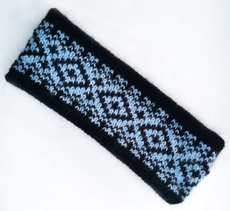 Großaufnahme eines selbstgestrickten, zweifarbigen Stirnbands in Schwarz und Hellblau im Fair-Isle-Strickmuster. Das doppellagige Norweger-Stirnband aus warmer Mohairwolle veranschaulicht das fertige Strickprojekt der kostenlosen Strickanleitung für ein Stirnband mit Zählschrift.