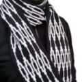 Oberk&ouml;rper einer Frau mit einem selbstgestrickten Schal im grafischen Schwarz-Wei&szlig;-Muster aus Merinowolle. Das Bild visualisiert das fertige Modell der kostenlosen Schritt-f&uuml;r-Schritt-Strickanleitung mit Z&auml;hlschrift zum Thema Schal im Grafikmuster stricken per Hand oder Strickmaschine.