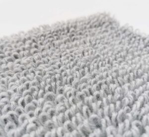 Auf dem Foto ist ein Strickstück in der Farbe Hellgrau-Melange zu sehen. Das Strickstück ist eine Maschenprobe eines Strickmusters. Genauer gesagt ist es eine Maschenprobe des Frotteemusters, das auch Schlingenmuster oder Schlaufenmuster genannt wird. Das Foto dient der Visualisierung der kostenlosen Strickanleitung "Frotteemuster, Schlingenmuster und Schlaufenmuster stricken".