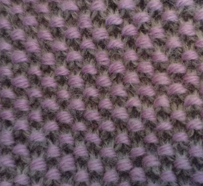 Dieses Foto zeigt eine Maschenprobe. Das Strickstück in den Farben Rosa und Beige ist der einzige Bildinhalt, es erstreckt sich über die gesamte Breite und Höhe des Bildes. Das Foto visualisiert die kostenlose Strickanleitung "Zweifarbiges Perlmuster stricken".