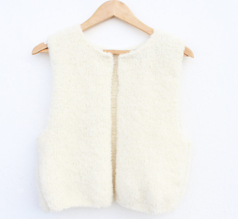 Selbstgestrickte, wollweiße Teddy-Weste für Damen, die sich gut zu verschiedenen Outfits kombinieren lässt. Das Modell aus weichem Merinogarn visualisiert die kostenlose Strickanleitung für eine kuschelige Teddyweste.